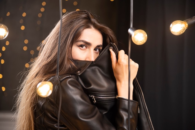 Portrait of a beautiful young model in black leather jacket posing near lamps.