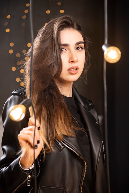 Портрет красивой молодой модели в черной кожаной куртке, позирующей возле ламп.