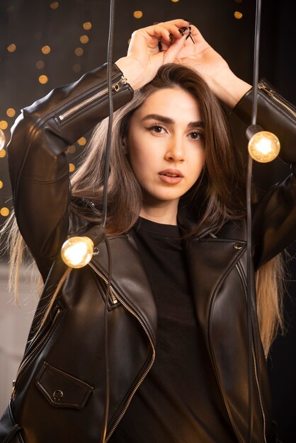 Portrait of a beautiful young model in black leather jacket posing near lamps.