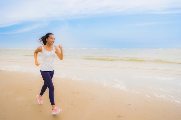 Esercizio asiatico della donna di bello giovane sport del ritratto eseguendo e pareggiando sulla spiaggia e sul mare all'aperto della natura