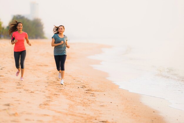 일출 또는 일몰 시간에 바다와 바다 근처 해변에서 세로 아름다운 젊은 스포츠 아시아 여자 실행 및 운동