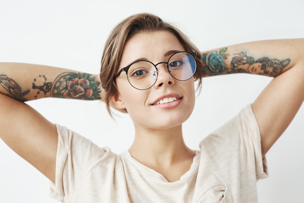 Portrait of beautiful young tattooed girl in glasses smiling .