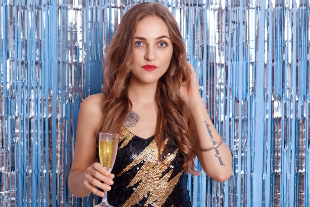 Ritratto di giovane e bella donna in un bellissimo abito da cocktail nero, ragazza con bicchiere di vino o champagne nelle sue mani