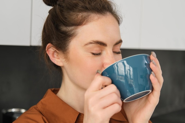 Portrait of beautiful young woman enjoying delicious aroma of freshly made coffee holding mug