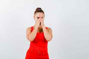 Free photo portrait of beautiful young woman holding hands on face in red tank top, pants and looking hopeful front view