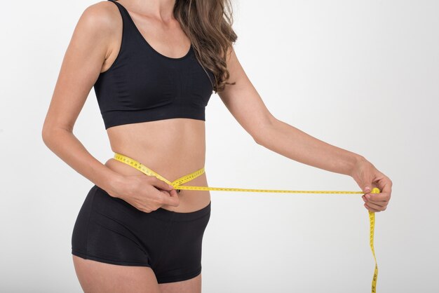 Portrait of beautiful young woman measuring her figure size with tape measure