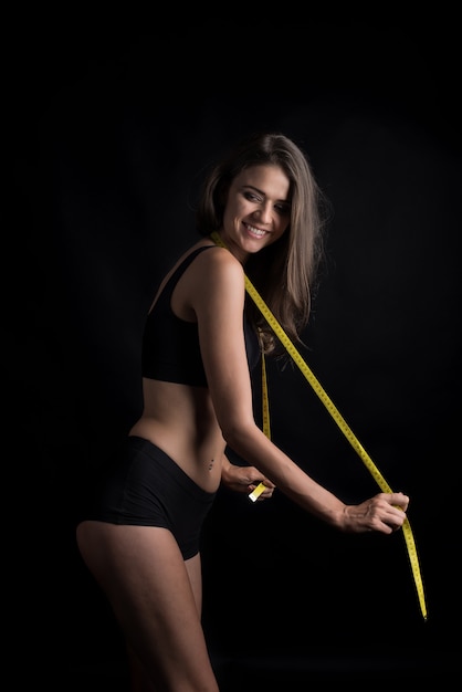 Free photo portrait of beautiful young woman measuring her figure size with tape measure