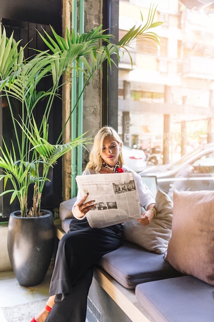 Портрет красивой молодой женщины, сидящей в кафе, читающей газету
