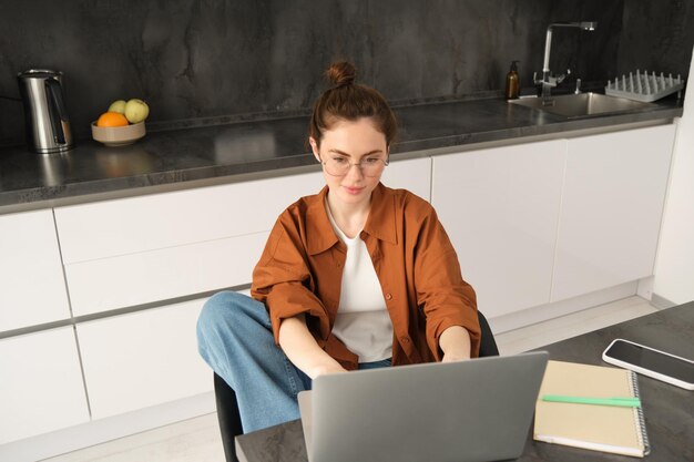 Foto gratuita ritratto di una bella giovane donna che studia a casa seduta con un laptop e documenti in cucina