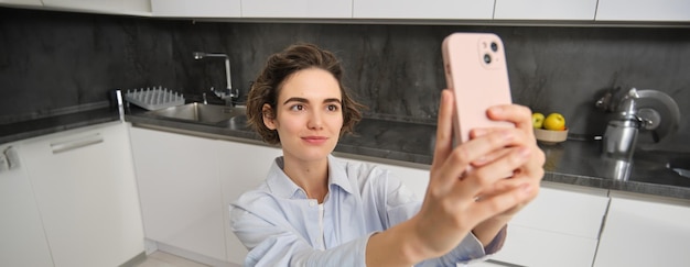 Free photo portrait of beautiful young woman taking selfie on mobile phone at home poses for photo with