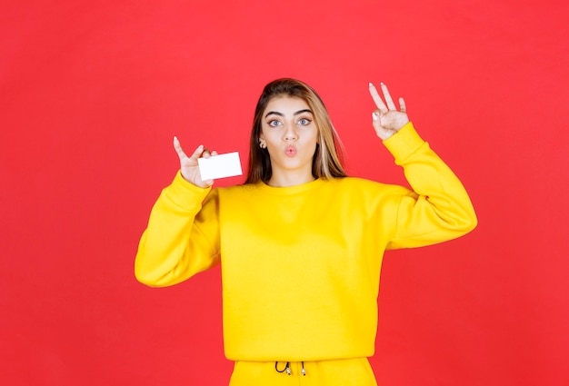 Portrait of beautiful young woman with blank business card giving ok sign
