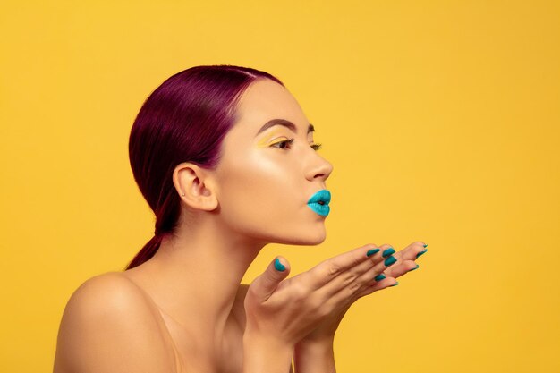 Portrait of beautiful young woman with bright make-up isolated on yellow studio