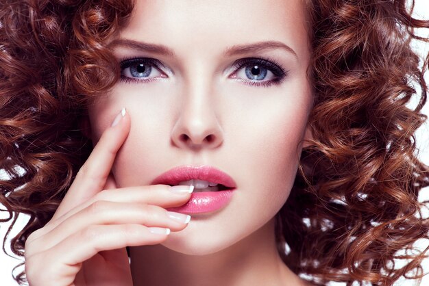 Portrait of beautiful young woman with brunette curly hair posing at studio. Closeup face with curly hairstyle, isolated on white.