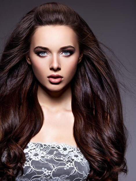 Portrait of the beautiful  young woman with long brown  hair posing  over dark wall