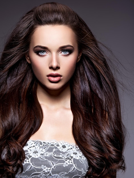 Portrait of the beautiful  young woman with long brown  hair posing  over dark wall