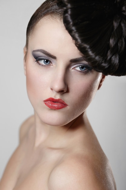 Portrait of beautiful young woman with red lips and unusual hair style on gray