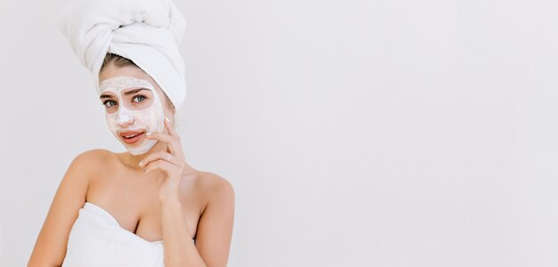 걸릴 목욕 후 수건으로 아름 다운 젊은 여자의 초상화는 그녀의 얼굴에 화장품 마스크를 확인합니다.
