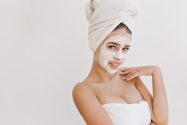 걸릴 목욕 후 수건으로 아름 다운 젊은 여자의 초상화는 그녀의 얼굴에 화장품 마스크를 확인합니다.