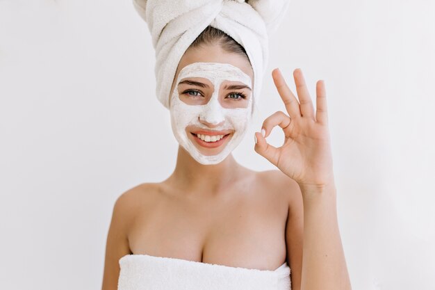 Портрет красивой молодой женщины с полотенцами после принятия ванны делает косметическую маску на лице.