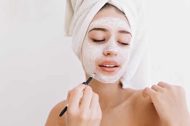 入浴後タオルで美しい若い女性の肖像画は、彼女の顔に化粧品のマスクを作ります。