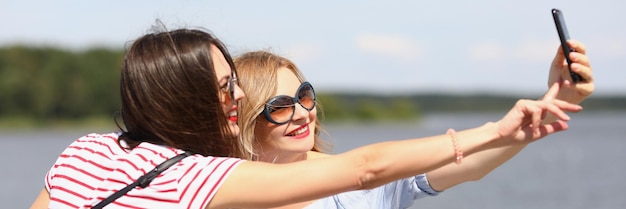 Portrait of best friends taking lovely selfie on smartphone smiling pretty women in bright