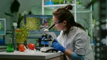Free photo portrait of biologist scientist in white coat working in expertise laboratory looking into microscope analyzing organic gmo leaf