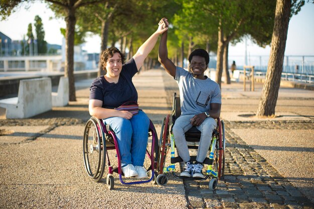 Портрет двухрасовой семьи на романтическом свидании в парке. Афроамериканец и кавказка в инвалидных колясках, держась за руки, улыбаясь. Любовь, отношения, концепция счастья