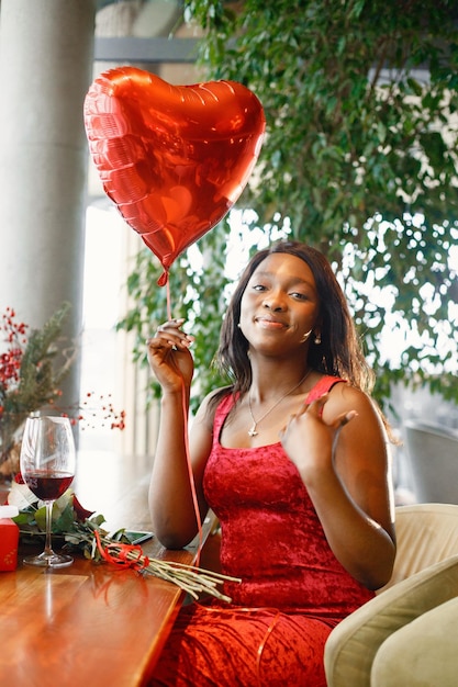 Portrait of a black woman holding a red heart balloon while sitting in restaurant