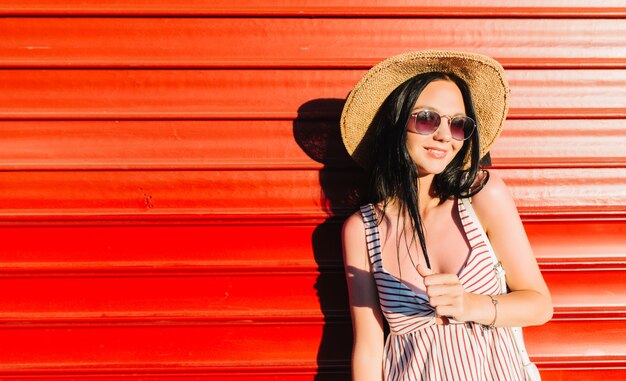 Portrait of blissful girl with black hair and gently smile, posing with pleasure in front of red wall