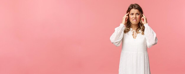 Portrait of blond upset and uneasy young woman have bad allergy on flowers at spring feel dizzy and suffer headache touch temples look away grimacing from painful migraine pink background