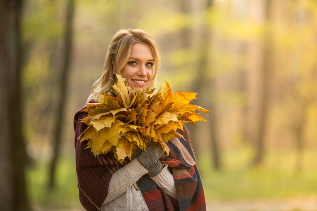 Portrait of blond woman standing with a bouquet from maple leaves Beautiful lady toothy smiling and looking at the camera