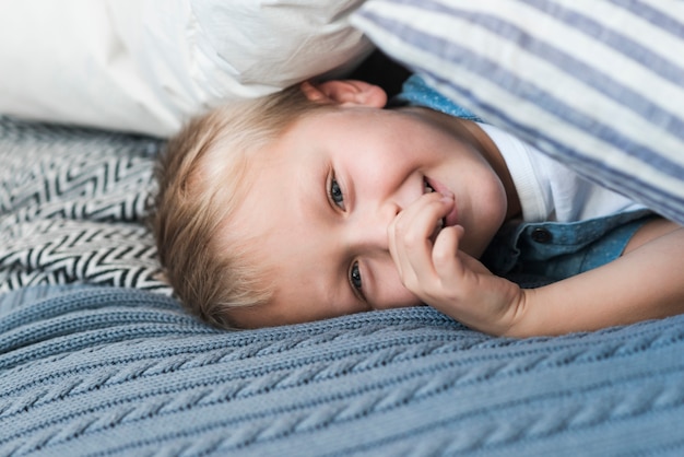Портрет блондинка мальчик, лежа на кровати с пальцем в рот