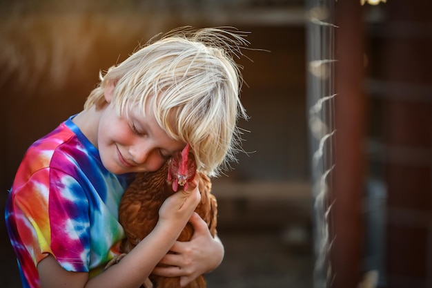 Portrait of a blonde Caucasian boy with a colorful shirt hugging a cute hen