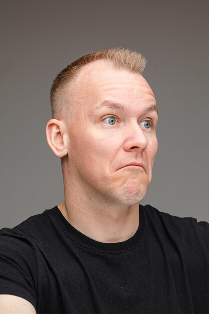 Portrait of blonde Caucasian man in black looking away with unsure facial expression showing uncertainty and confusion.