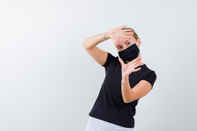 Portrait of blonde lady making frame gesture in black t-shirt isolated