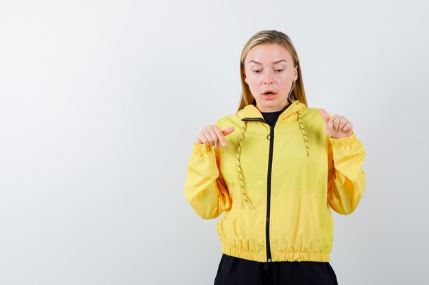 Portrait of blonde lady pointing down in tracksuit and looking wondered front view