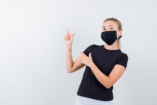 Portrait of blonde lady pointing at upper left corner in black t-shirt isolated