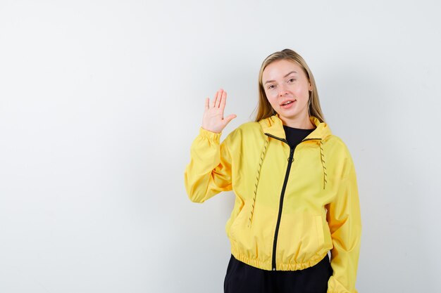 Portrait of blonde lady showing palm in tracksuit and looking merry front view