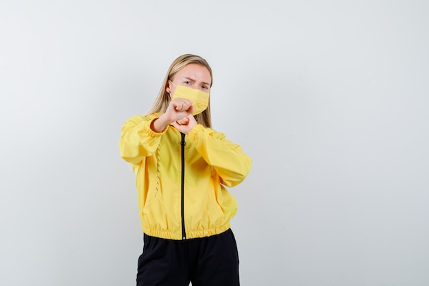 Portrait of blonde lady standing in fight pose in tracksuit, mask and looking serious front view