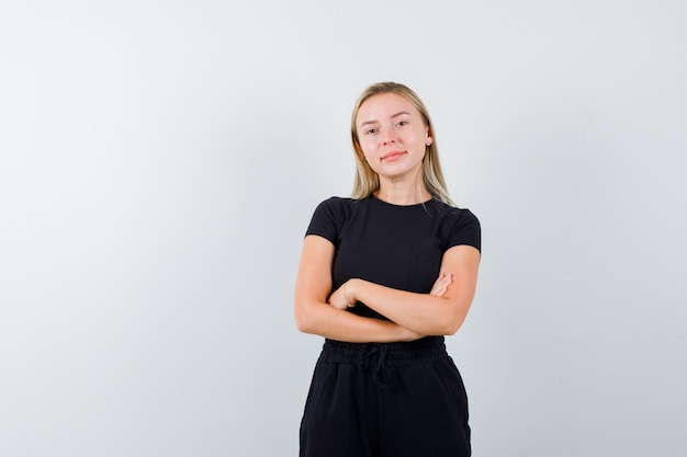 Free photo portrait of blonde lady standing with crossed arms in black dress and looking proud front view