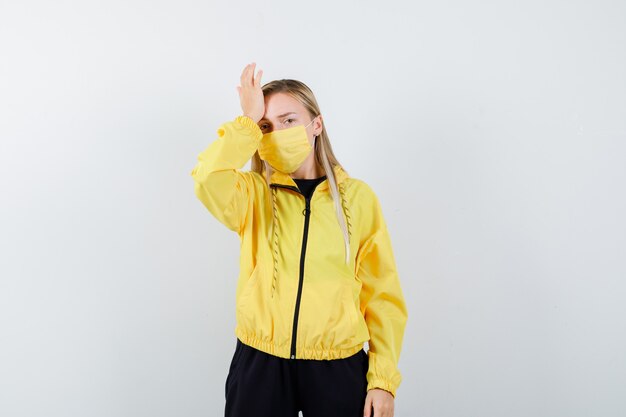 Portrait of blonde lady suffering from headache in tracksuit, mask and looking tired front view