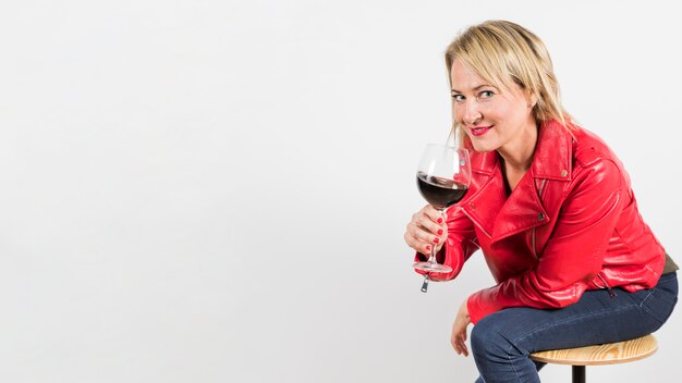 Portrait of a blonde mature woman holding red wine glass in hand isolated on white background