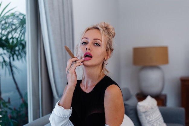 Portrait of blonde woman in body suit and white shirt with pink beautiful lips holding cigar