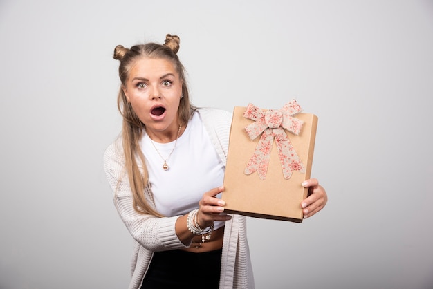 Portrait of blonde woman holding gift with surprised expression.