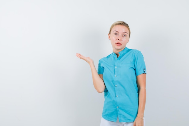 Free photo portrait of blonde woman pretending to show something in blue blouse isolated