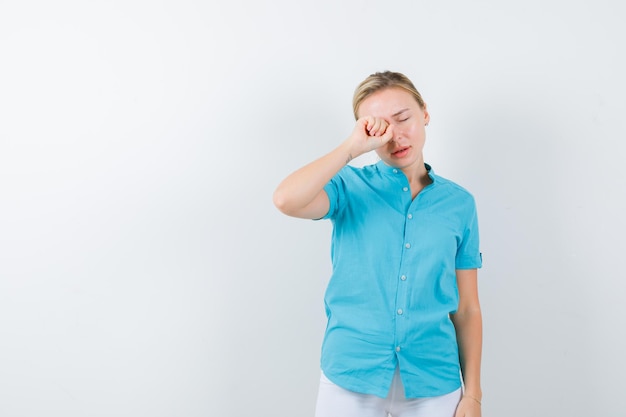 Ritratto di donna bionda che si sfrega gli occhi mentre piange in camicetta blu isolata