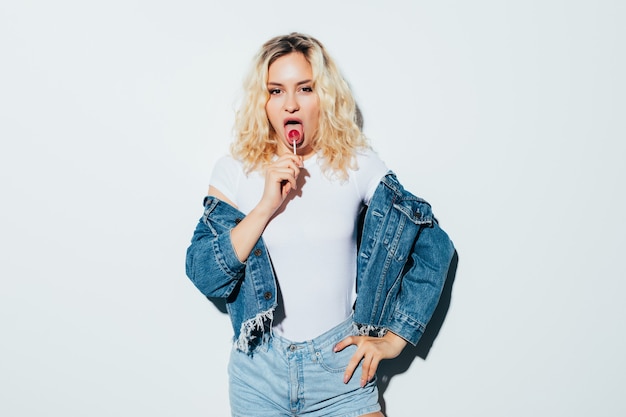 Free photo portrait of blonde woman wearing holding candy, isolated on white wall