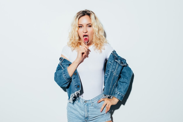 Portrait of blonde woman wearing holding candy, isolated on white wall