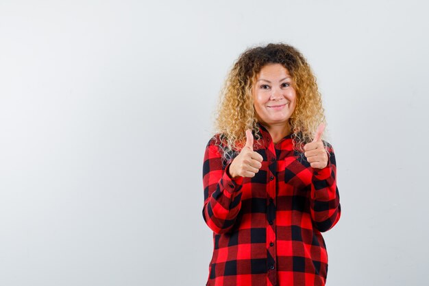 Foto gratuita ritratto di donna bionda con i capelli ricci che mostra il doppio pollice in su in camicia a quadri e sembra una vista frontale soddisfatta