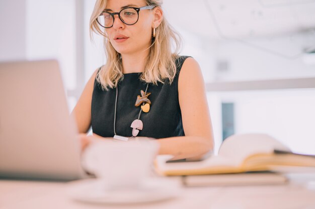 Портрет блондинка молодой предприниматель, глядя на ноутбук в офисе
